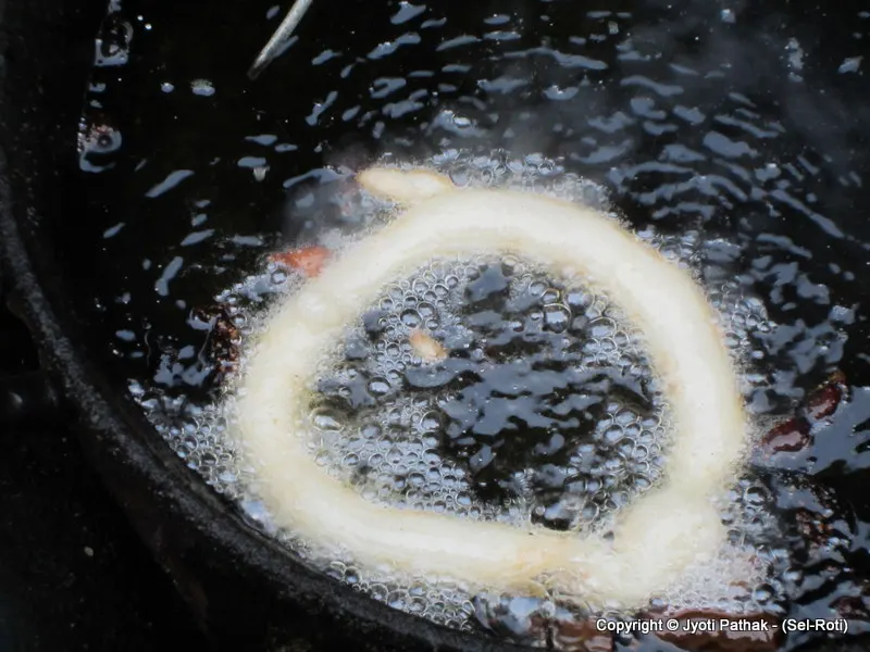 The batter puffs up and rises as it cooks. She pushes it into the oil frequently with the back of a spoon.