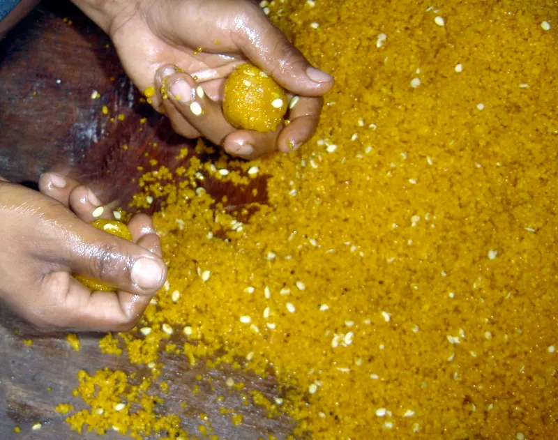 In this picture, a sweet maker is busy with a special order of Motichur ko Laddu for a religious function - working with a small handful of the chickpeas laddu mixture, he is rolling and squeezing between his palm to form 1-inch balls.