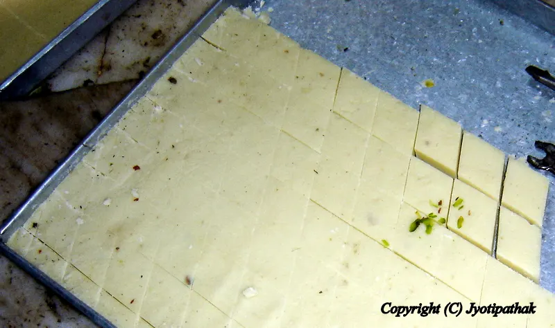 The sweet maker is showing me how to cut the sheet of Burfi into diamond shape. He first cut the sheets into several lengthwise pieces. He then cuts each pieces into diamond shape by using a thin, sharp knife.