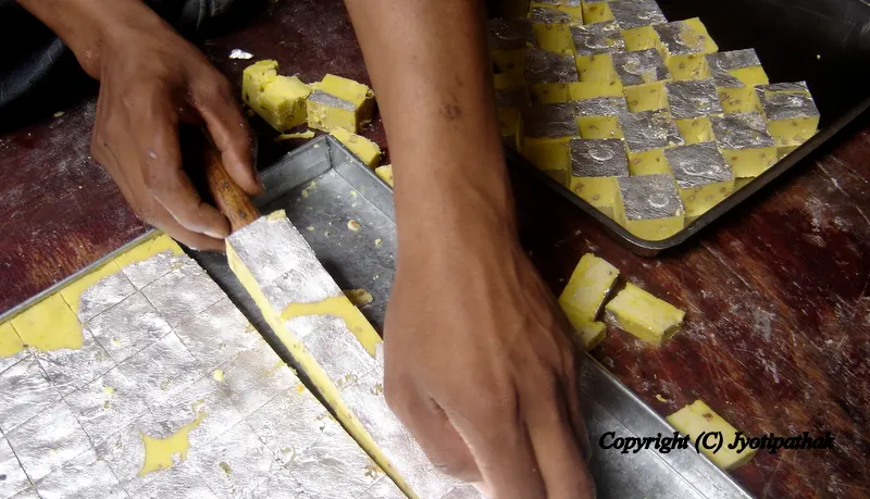 After applying a layer of varak paper (silver leaf) on top of the sweets, he cuts the sheets into attractive square pieces, then arranges into a tray to create a professional finish. The tray will be transferred to the shop window for sale.