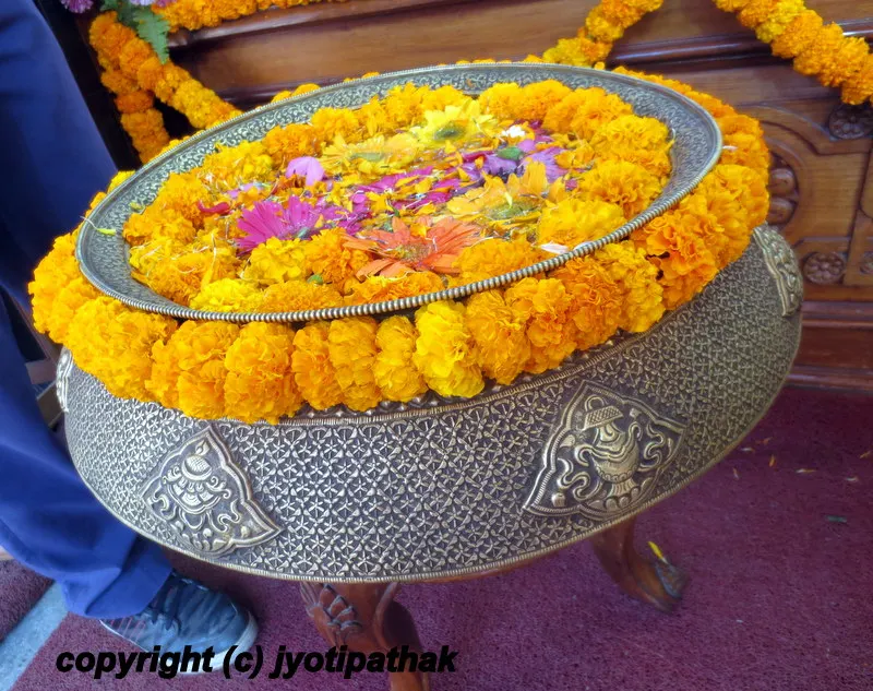 ... garlands of Marigold and floating petals of flowers adorn this beautiful brass pot with astamangal (eight auspicious signs) which is made by old world artisan techniques in Nepal.