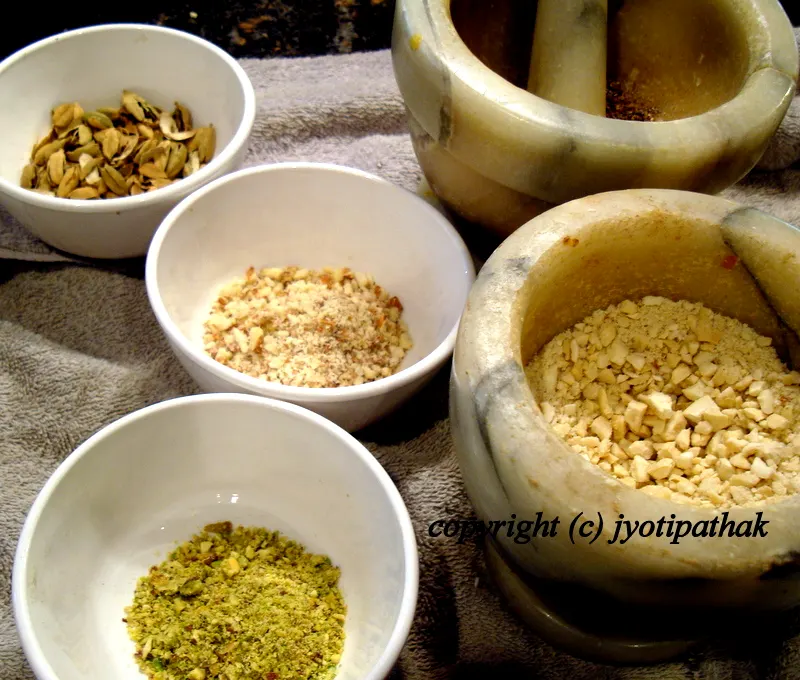 ... coarsely grinding a small amount of nuts in a mortar and pestle and the green cardamom seeds is getting ready to be grind into fine powder.