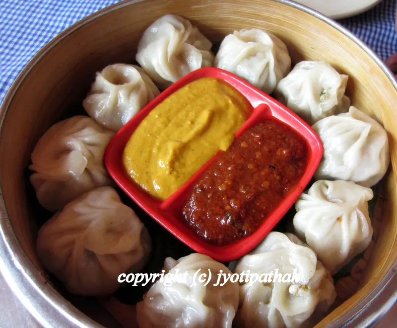 A traditional serving of meat-filled Momo dumplings, brimming with delicate and flavorful juices served with traditional tomato chutney and yellow chili-tomato-sesame seed sauce.