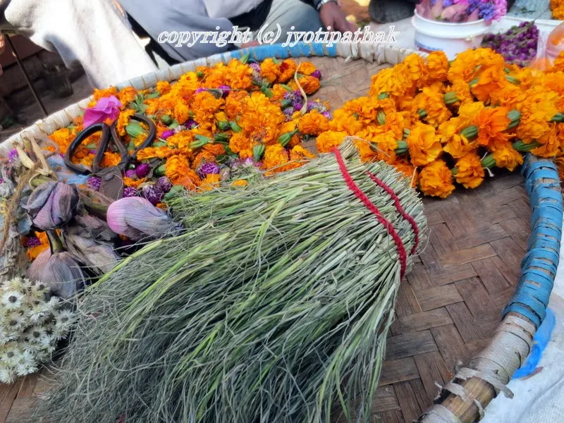 Vendor is selling simple dubo grass and marigold flower garland, lotus flower buds and other flowers for religious offerings in front of a temple in Kathmandu.