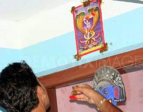 Nag Panchami celebration - Nepalese devote is sticking a picture of a snake god above the doorways of a house with a offering of dubo grass, rice and red vermillion powder on the occasion of Nag Panchami. Photo courtesy.