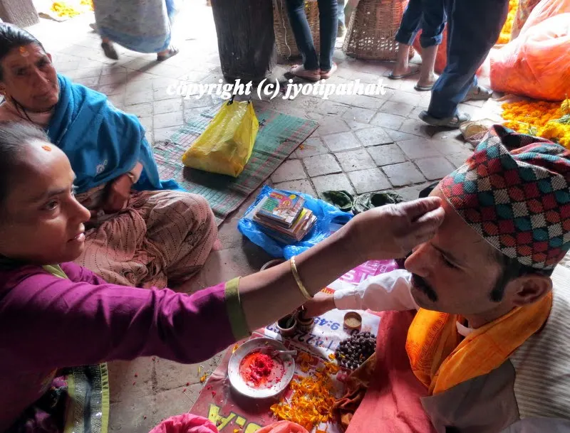 Image of two women putting tikaa on the forehead of a priest